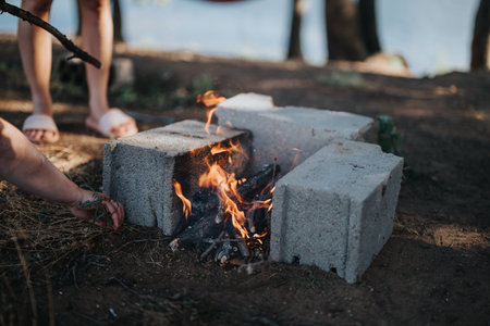 Group of people preparing a barbeque fire in a rustic outdoor setting near a lake