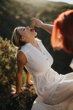 Young woman enjoying fresh berries outdoors, hand feeding in natureの写真素材