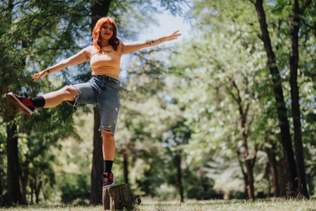 Young woman balancing on tree stump in park with arms outstretched enjoying a summer dayの写真素材