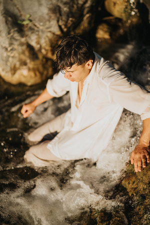 Young man in white shirt relaxing in a flowing stream