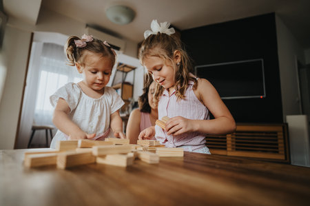 Young sisters playing with wooden blocks at home engaging in creative family timeの写真素材