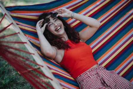 Happy woman relaxing in a colorful hammock outdoors, enjoying a sunny day and laughing with joyの写真素材