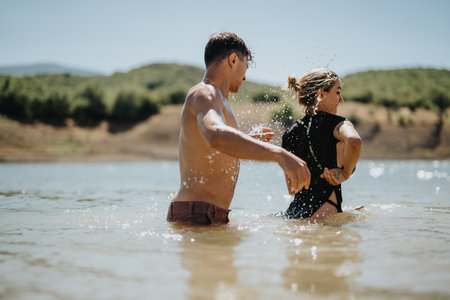 Young couple enjoying summer day by playing and splashing water at the lakeの写真素材