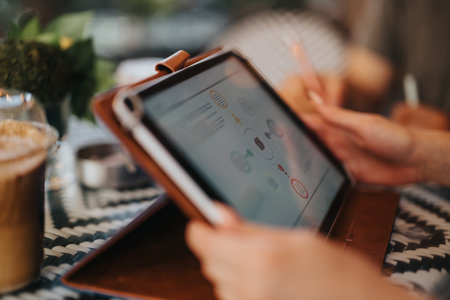 Business meeting in coffee shop with tablet and notepad, focus on screen and handsの写真素材