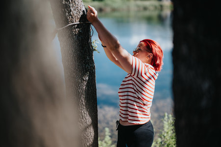Woman setting up hammock between trees by a lake on a sunny day
