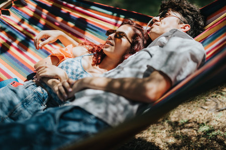 Young couple relaxing together in a colorful hammock on a sunny day outdoorsの写真素材