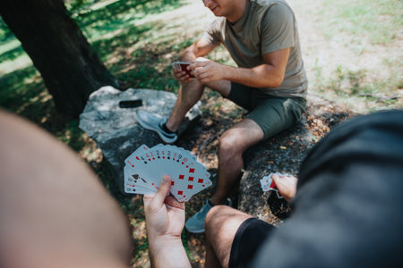 Friends playing cards outdoors on a sunny day in the parkの写真素材