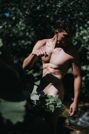 Muscular man in nature surrounded by large green leaves in dappled sunlightの写真素材