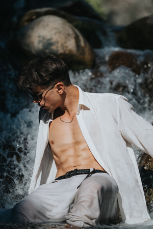 Confident young man in white shirt sitting by a waterfallの写真素材