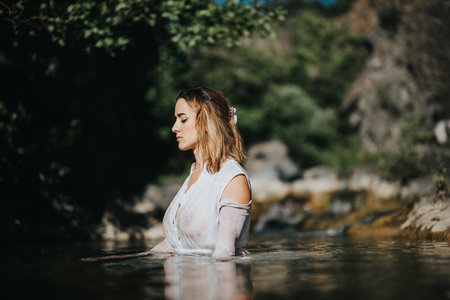 Pensive young woman standing in a serene river surrounded by natureの写真素材