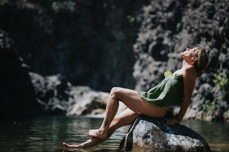 Young woman relaxing on a rock by the river in a natural settingの写真素材