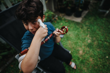 Young child confidently handling colorful snakes outdoors in gardenの写真素材