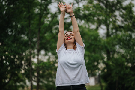 Joyful woman stretching arms in a lush green park settingの写真素材