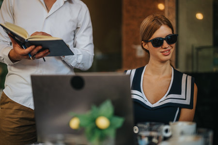 Businesspeople collaborating outdoors with laptop and notebook, engaging in a lively discussion at a cafe table.の写真素材