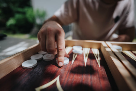 Close-up of a hand playing backgammon outdoors on a sunny day, focusing on the strategic placement of pieces on the wooden board.の写真素材