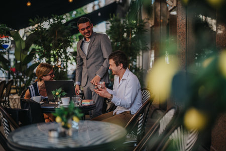 Casual business meeting in outdoor cafe with happy businesspeople discussing work over coffee and laptopsの写真素材