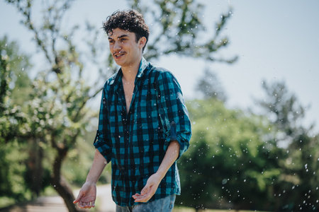 Happy young man enjoying water splashes on a sunny day in the park