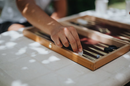 Close-up of a person playing a relaxing game of backgammon outdoors on a sunny day, capturing a...