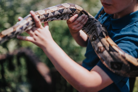 Young girl playfully interacts with large pet snake in outdoor settingの写真素材