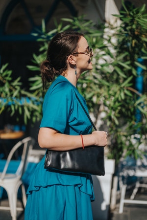 Woman in blue dress with a black purse enjoying a sunny day outdoorsの写真素材