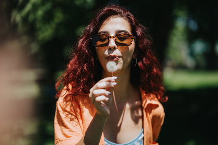 Young woman enjoying a sunny day in the park blowing dandelion seeds