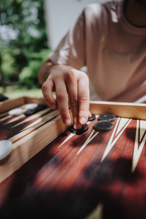 Close-up of a person playing backgammon outdoors, focusing on hand movement and strategy during a sunny dayの写真素材