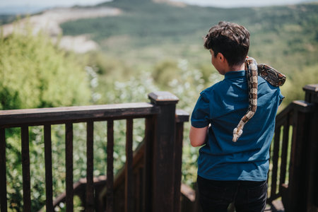 Child interacting with a pet snake outdoors on a sunny dayの写真素材