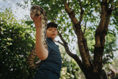 Young girl confidently holding a large snake outdoors in natureの写真素材