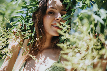 Young woman smiling through green foliage on a sunny day in natureの写真素材