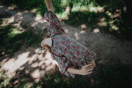 Girl performing modern dance in nature, wearing floral dress, expressive movement under sunlightの写真素材