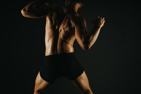 Muscular man showing his back muscles in black shorts, highlighting fitness and strengthの写真素材