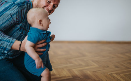 Father joyfully supporting baby taking first steps at homeの写真素材