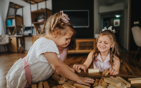 Mother playing with her little daughters at home building blocks and having fun togetherの写真素材
