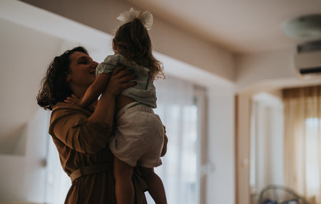 Loving mom holding her daughter in a cozy home settingの写真素材