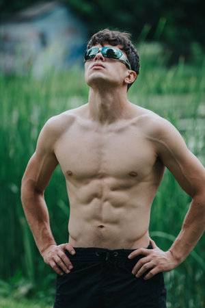 Fit young man posing shirtless outdoors with sunglasses and athletic physiqueの写真素材