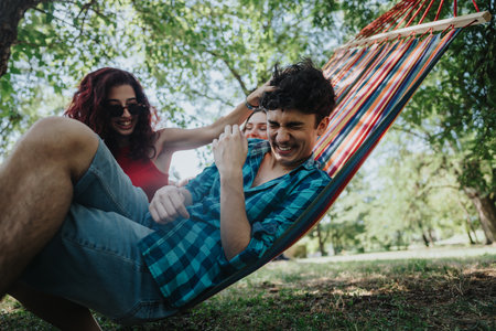 Friends having fun and laughing on a hammock in the park on a sunny dayの写真素材
