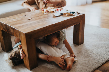 Playful children hiding under a wooden table in family living roomの写真素材