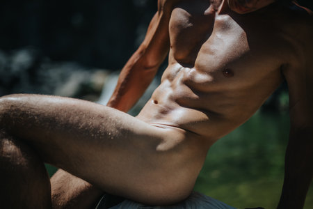 Athletic muscular male sunbathing outdoors by a scenic body of waterの写真素材