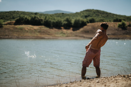Man enjoying a lake throwing stones on a sunny day in natureの写真素材