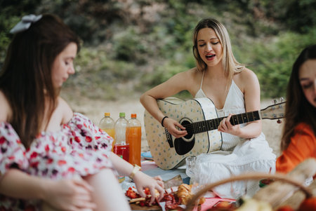 Young women enjoying a picnic with guitar music amidst natureの写真素材