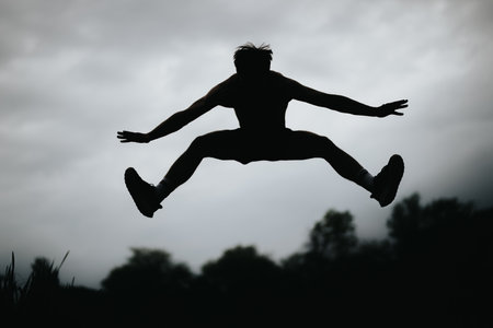 Man practicing high jumps against cloudy sky in an outdoor settingの写真素材