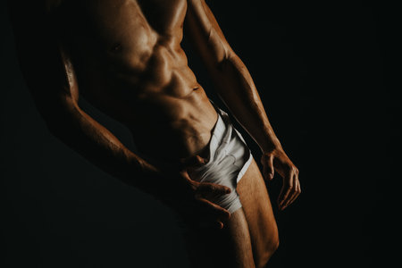 Muscular man showcasing physique in low-key lighting for fitness, bodybuilding, and strength conceptsの写真素材