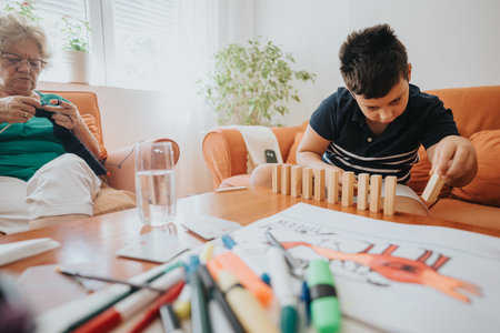 Grandmother knitting while young boy plays with building blocks at home