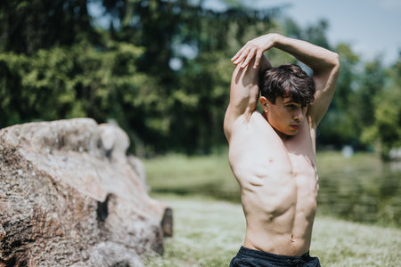 Young man performing stretching exercises outdoors in a park setting on a sunny dayの写真素材