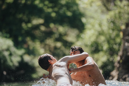 Two friends wrestling playfully in a river on a sunny dayの写真素材