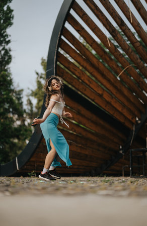 Young girl performing modern dance movements in green park with expressive posture under unique architectural structureの写真素材