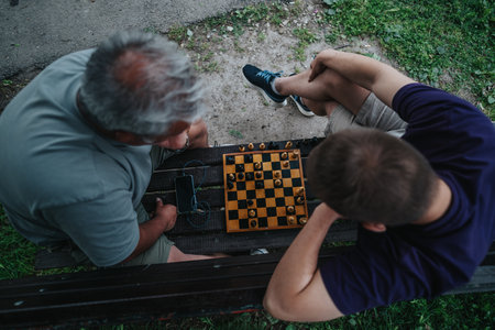 Two men playing chess outdoors on a wooden bench
