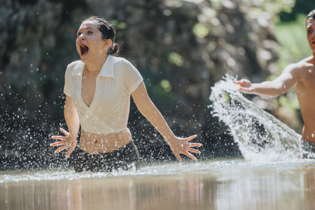 Joyful woman surprised by playful splash in a sunny riverの写真素材