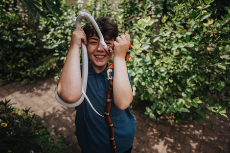 Young girl happily playing with two colorful snakes outdoorsの写真素材