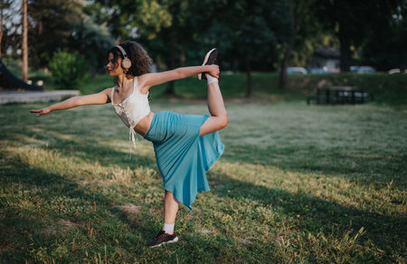 Young girl warming up with dance moves in a sunny park settingの写真素材